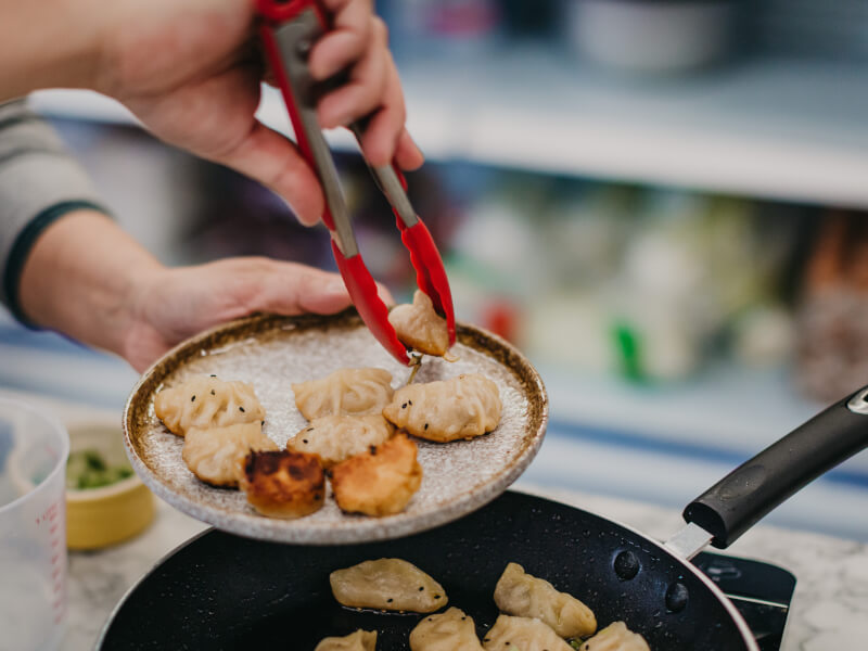 Close up of a person placing Chinese dumplings on a plate using tongs